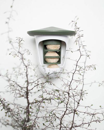 Distributeur de nourriture pour oiseaux avec plusieurs compartiments et un toit vert, accroché à un mur blanc.